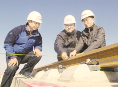 ●余霖（中）在兰新高铁施工现场检查接触网基础限界。 （王健/摄）
