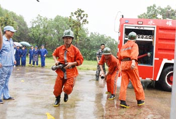 图为职工和消防人员在大雨中进行火灾扑救和逃生演练。