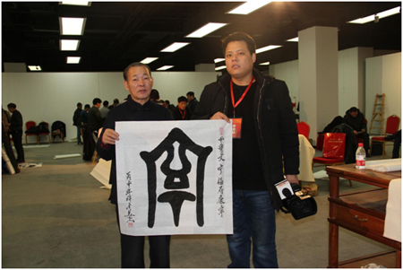 国际著名书画艺术大师许金美(左)赠送给中国中央电视台摄影记者(右)一幅甲骨文书法作品“宁”，并合影留念。